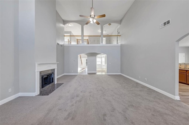 unfurnished living room featuring light carpet, a high ceiling, sink, ceiling fan, and a premium fireplace