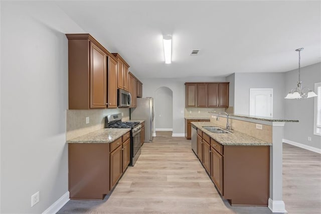 kitchen featuring light stone counters, stainless steel appliances, sink, pendant lighting, and a notable chandelier