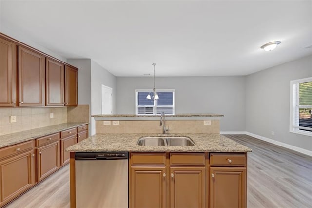 kitchen with light wood-type flooring, tasteful backsplash, stainless steel dishwasher, sink, and hanging light fixtures