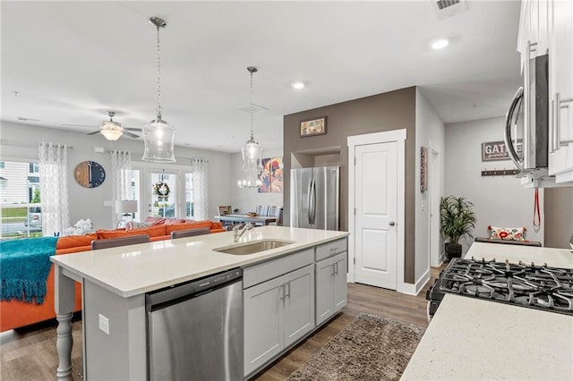 kitchen with appliances with stainless steel finishes, a sink, light countertops, a center island with sink, and dark wood-style floors