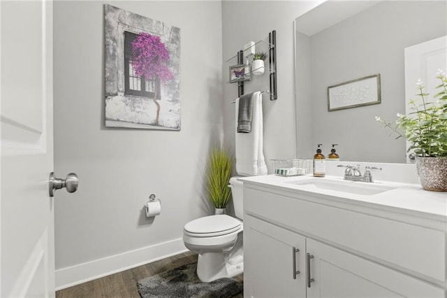 half bathroom with wood finished floors, toilet, baseboards, and vanity