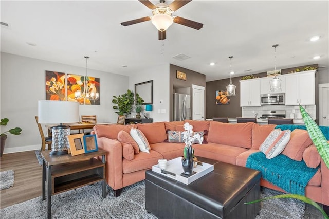 living area with recessed lighting, wood finished floors, a ceiling fan, baseboards, and a chandelier