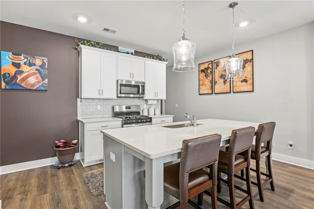 kitchen featuring appliances with stainless steel finishes, baseboards, dark wood-style floors, an island with sink, and a breakfast bar