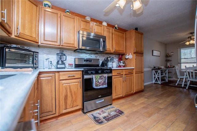 kitchen with appliances with stainless steel finishes, decorative backsplash, ceiling fan, and light hardwood / wood-style flooring