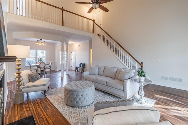 living room with a towering ceiling, ornamental molding, hardwood / wood-style flooring, decorative columns, and ceiling fan with notable chandelier