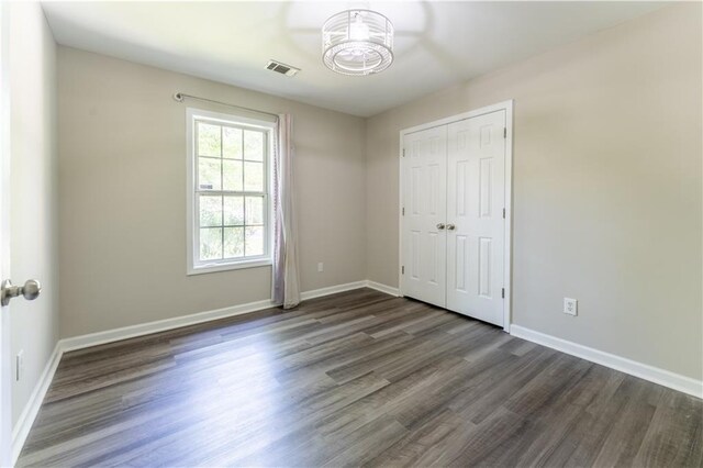unfurnished bedroom with dark wood-type flooring, visible vents, baseboards, and an inviting chandelier