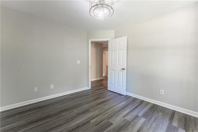 unfurnished room with dark wood finished floors, baseboards, and a chandelier
