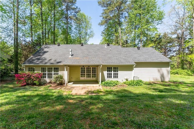 rear view of property with a lawn, a shingled roof, and a patio