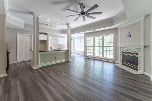 unfurnished living room featuring a raised ceiling, a ceiling fan, crown molding, and decorative columns