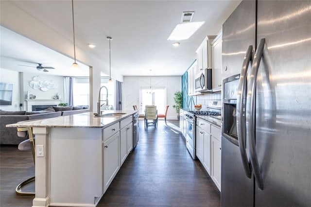 kitchen featuring a kitchen island with sink, hanging light fixtures, sink, white cabinetry, and stainless steel appliances