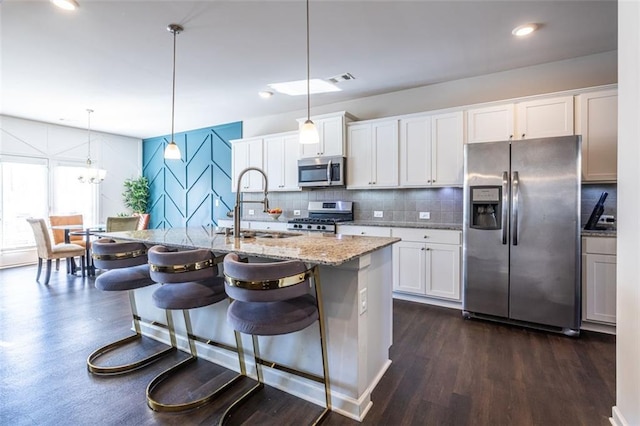 kitchen featuring stainless steel appliances, a kitchen island with sink, pendant lighting, white cabinets, and a breakfast bar area