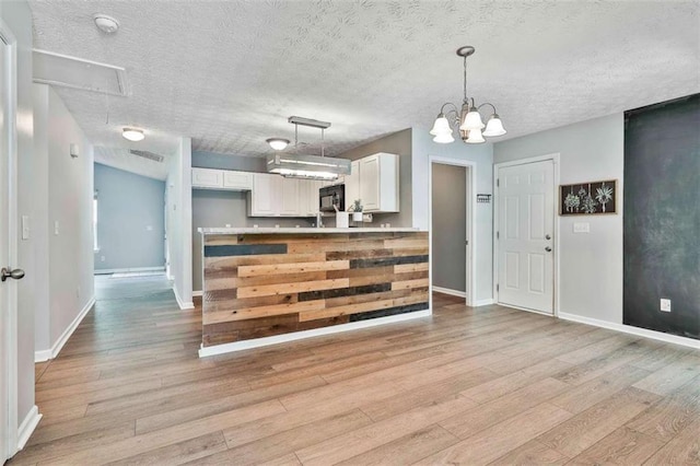 2551 Luther Bailey Rd, Senoia, GA 30276 - kitchen featuring light wood-style flooring, white cabinetry, black microwave, decorative light fixtures, and a textured ceiling