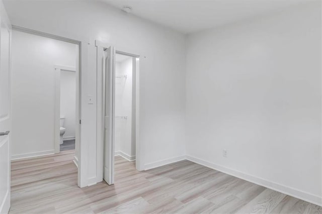 unfurnished bedroom with light wood finished floors, a closet, ensuite bath, and baseboards