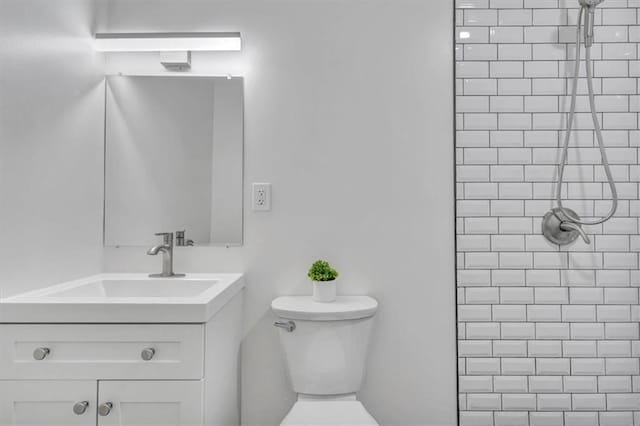 bathroom featuring a tile shower, toilet, and vanity