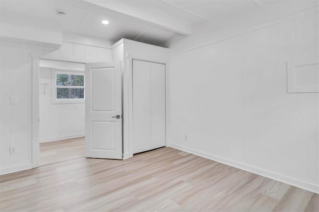 unfurnished bedroom featuring light wood finished floors, beamed ceiling, a closet, and baseboards