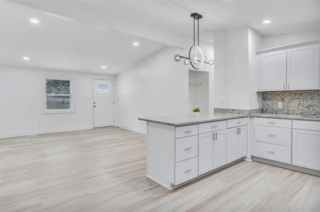 kitchen featuring light wood-style floors, a peninsula, light stone counters, and tasteful backsplash