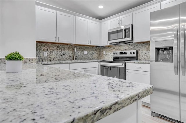 kitchen with tasteful backsplash, white cabinets, stainless steel appliances, and light stone counters