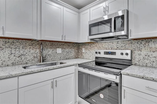 kitchen featuring stainless steel appliances, decorative backsplash, white cabinetry, a sink, and light stone countertops