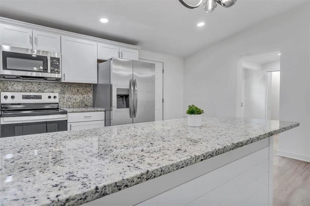 kitchen with light stone counters, white cabinets, appliances with stainless steel finishes, and light wood-style floors