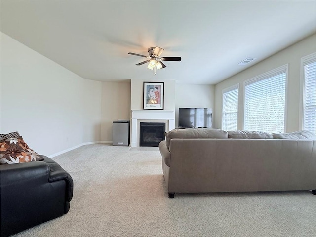 living room with carpet flooring, baseboards, ceiling fan, visible vents, and a glass covered fireplace