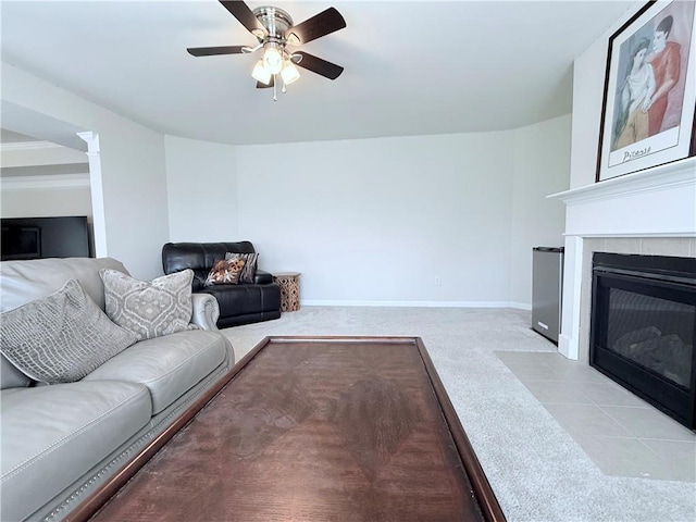 living area with baseboards, carpet flooring, a tile fireplace, and a ceiling fan
