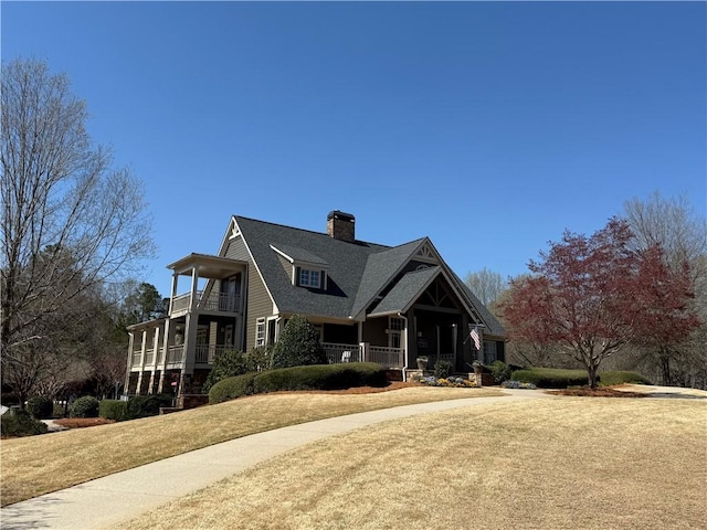 view of front facade featuring a balcony, a front lawn, and a chimney