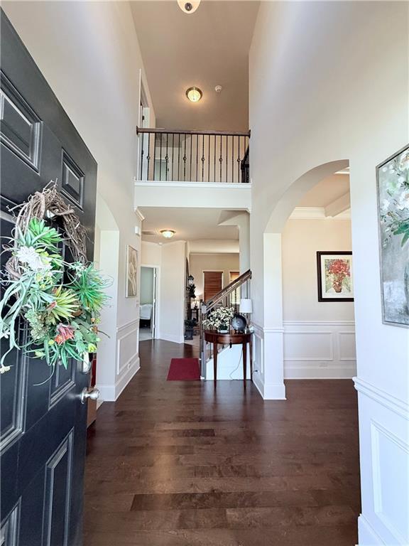 foyer with a decorative wall, a towering ceiling, wood finished floors, stairway, and arched walkways