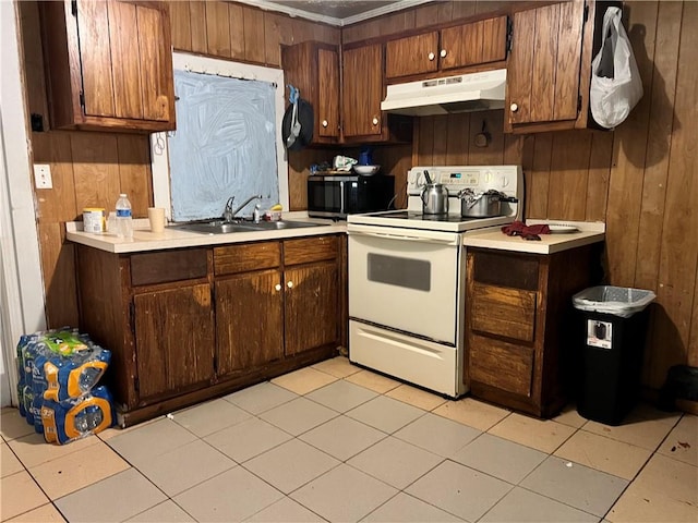 kitchen with sink, white electric range, light tile patterned flooring, and wood walls