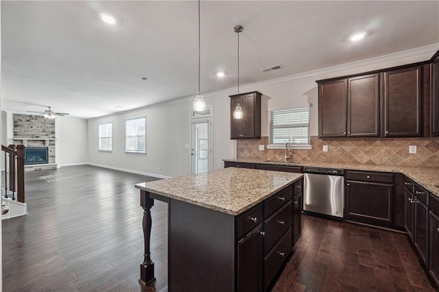 kitchen featuring pendant lighting, dark wood-type flooring, a stone fireplace, stainless steel dishwasher, and a kitchen island