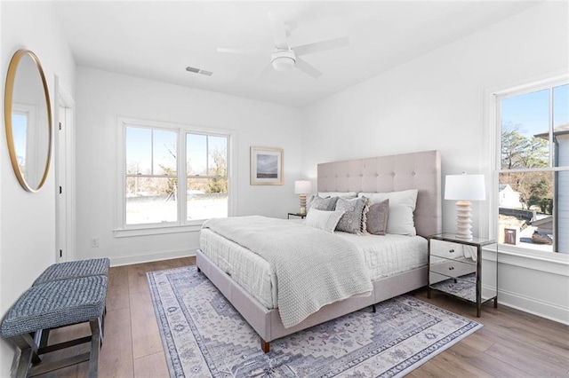 bedroom featuring ceiling fan, visible vents, baseboards, and wood finished floors