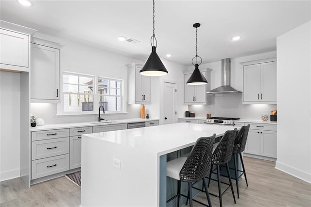 kitchen with a center island, wall chimney exhaust hood, a sink, light countertops, and light wood-style flooring