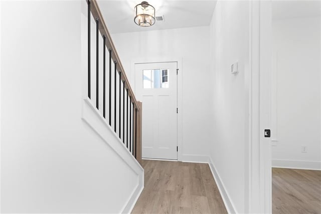 foyer entrance with a chandelier, light wood finished floors, and baseboards