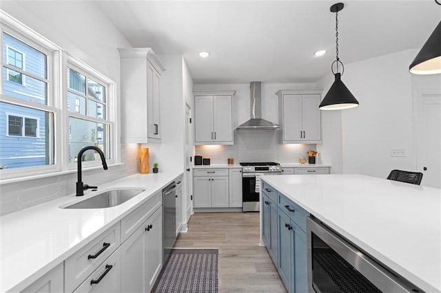 kitchen with pendant lighting, wall chimney range hood, light countertops, a sink, and stainless steel appliances