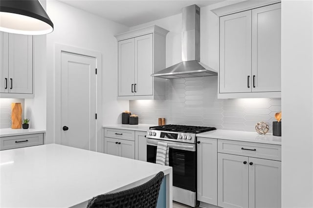 kitchen with wall chimney range hood, light countertops, stainless steel gas stove, and backsplash