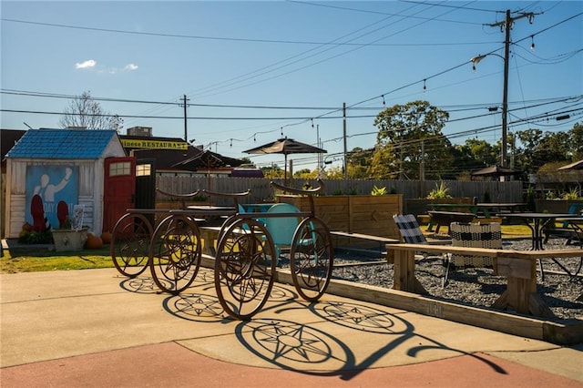 view of playground featuring outdoor dining space, a patio, a shed, an outbuilding, and fence
