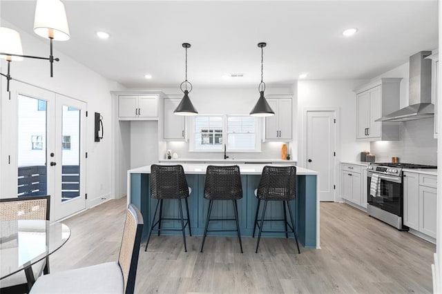 kitchen with wall chimney exhaust hood, a center island, stainless steel gas range, light countertops, and light wood finished floors