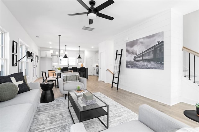 living room with light wood-type flooring, recessed lighting, stairway, visible vents, and ceiling fan with notable chandelier