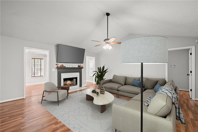 living room featuring a high end fireplace, hardwood / wood-style floors, vaulted ceiling, and ceiling fan