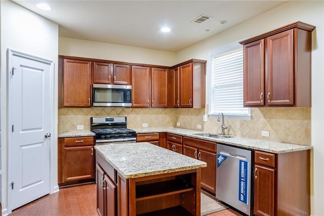 kitchen featuring sink, appliances with stainless steel finishes, light stone countertops, a kitchen island, and light wood-type flooring