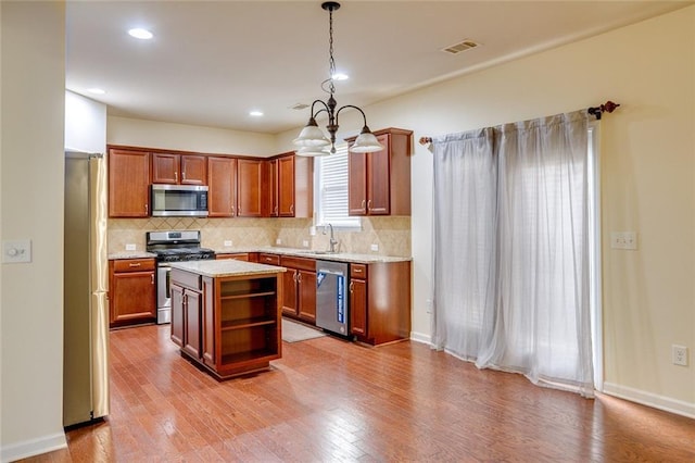 kitchen with a kitchen island, decorative light fixtures, sink, stainless steel appliances, and light wood-type flooring