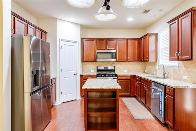 kitchen featuring sink, stainless steel appliances, a center island, decorative light fixtures, and light wood-type flooring