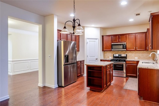 kitchen with sink, hanging light fixtures, stainless steel appliances, light stone countertops, and a kitchen island