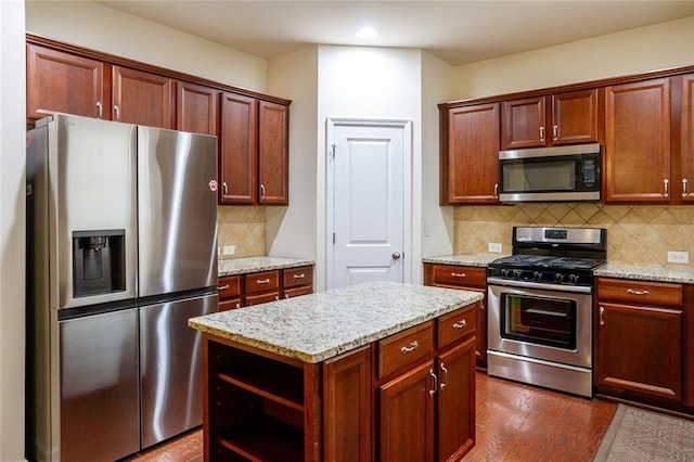 kitchen with stainless steel appliances, light stone countertops, a kitchen island, and backsplash