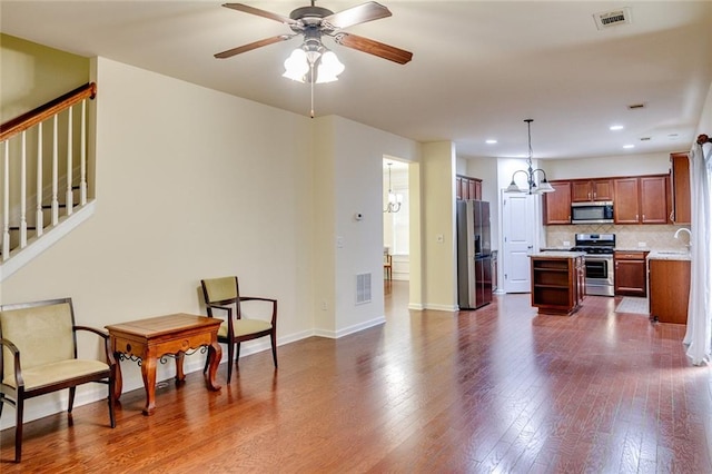 kitchen with decorative light fixtures, appliances with stainless steel finishes, hardwood / wood-style floors, ceiling fan with notable chandelier, and decorative backsplash