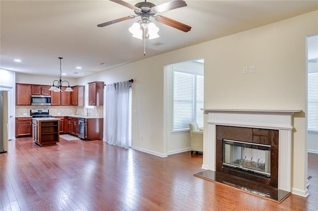 kitchen with tasteful backsplash, decorative light fixtures, a kitchen island, stainless steel appliances, and hardwood / wood-style floors