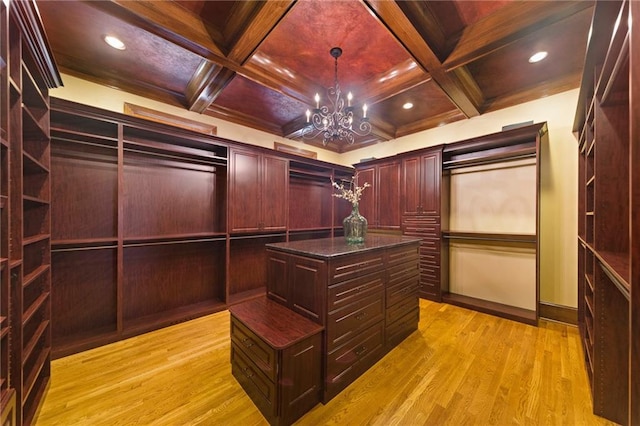 walk in closet featuring coffered ceiling, an inviting chandelier, and light hardwood / wood-style floors