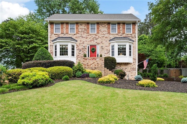 colonial inspired home featuring brick siding, a front lawn, and fence