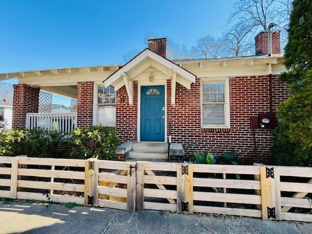 view of front of house with a fenced front yard, entry steps, brick siding, and a chimney