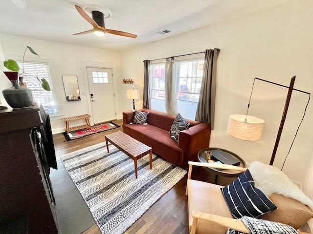 living area featuring ceiling fan, visible vents, dark wood-style flooring, and a wealth of natural light