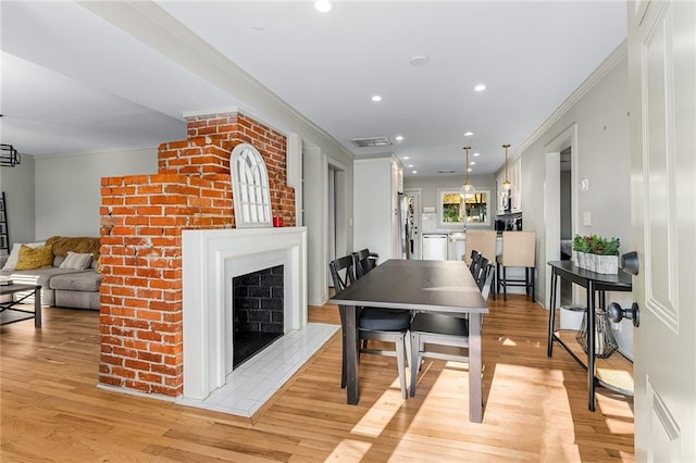 dining area featuring a fireplace, light hardwood / wood-style floors, and crown molding